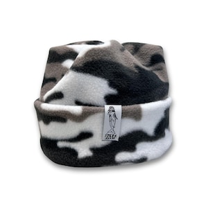 May include: A camouflage-patterned beanie hat in shades of black, white, and gray. The hat features a folded brim and a small tag with a logo. The hat is made of a soft, possibly fleece-like material.