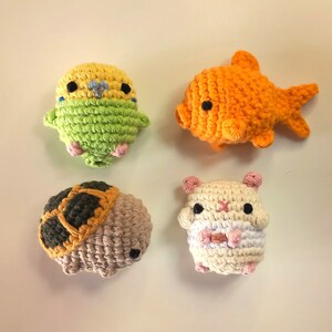 May include: Four crocheted stuffed toys: a yellow and green parakeet, an orange goldfish, a brown and tan turtle, and a white hamster with pink accents.