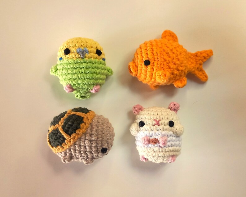 May include: Four crocheted stuffed toys: a yellow and green parakeet, an orange goldfish, a brown and tan turtle, and a white hamster with pink accents.