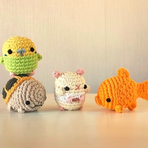 May include: Four crocheted stuffed animals: a yellow and green parakeet, a brown turtle, a white hamster, and an orange goldfish.