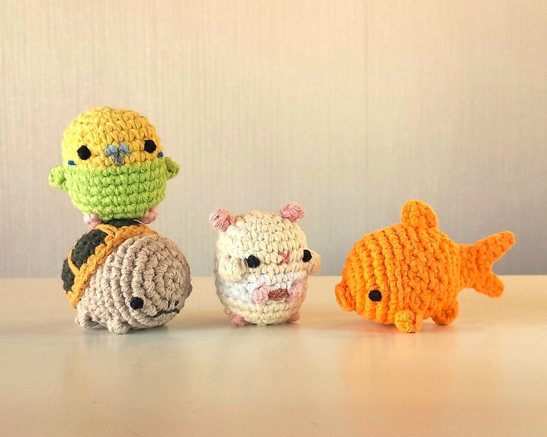 May include: Four crocheted stuffed animals: a yellow and green parakeet, a brown turtle, a white hamster, and an orange goldfish.