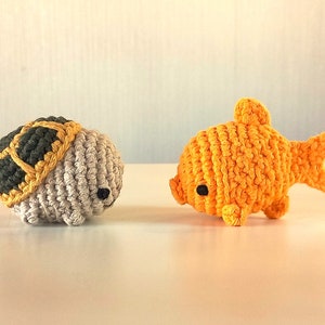 May include: A crocheted turtle with a grey shell and yellow accents, and a crocheted goldfish with orange scales and black eyes.