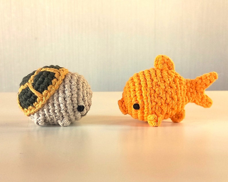 May include: A crocheted turtle with a grey shell and yellow accents, and a crocheted goldfish with orange scales and black eyes.