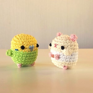May include: A crocheted yellow and green bird and a crocheted white and pink hamster. Both are small and have black eyes.