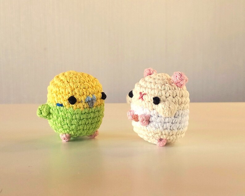 May include: A crocheted yellow and green bird and a crocheted white and pink hamster. Both are small and have black eyes.