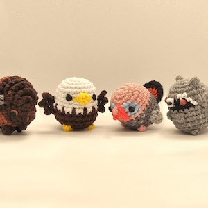 May include: Four handmade crochet animal figures: a brown and orange bison, a white and brown eagle with yellow beak, a pink and grey turkey, and a grey raccoon with a black mask. These plush toys are suitable for children or as decorative items.