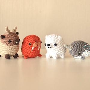 Puede incluir: Cuatro animales de peluche de crochet: un reno marrón, una morsa naranja, un oso polar blanco y una narval gris.