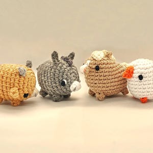 May include: Four handmade crochet animal toys: a yellow pig, a gray donkey, a tan sheep, and a white duck with orange accents. Each toy has black eyes and is made with textured yarn, showcasing a whimsical, handcrafted style.