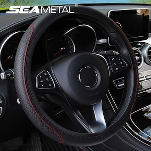 May include: Black steering wheel cover with red stitching. The cover has a diamond pattern on the sides and the text "SEAMETAL" at the top. The steering wheel has buttons and a silver center.