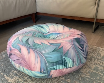 Puede incluir: Un cojín de suelo redondo con estampado floral en colores rosa, azul y verde. El cojín está hecho de tela y tiene una textura suave y cómoda.