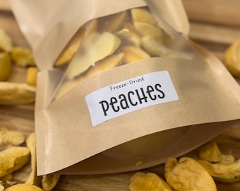 May include: A clear plastic bag filled with freeze-dried peach slices, labeled "Peaches." The bag is inside a brown paper bag, with additional peach slices scattered on a wooden surface. The peaches are a light yellow color.