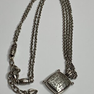 May include: Silver necklace with a square pendant, decorated with a floral pattern. The pendant hangs from a fine chain with an adjustable clasp. A classic piece of jewellery.