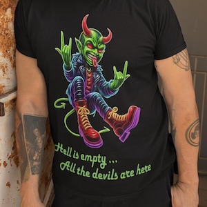 Puede incluir: Camiseta negra con un diablo de dibujos animados con cuernos rojos, piel verde y una chaqueta de cuero. El diablo hace un gesto de rock and roll con la mano. El texto de la camiseta dice: "Hell is empty... All the devils are here."