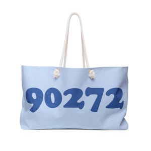 May include: A light blue tote bag with the number "90272" printed in dark blue. The bag has white rope handles and is designed for carrying items. The bag is made of a soft material.