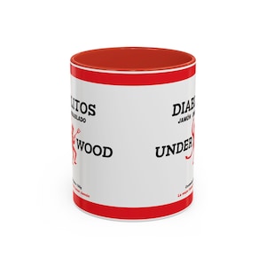 Puede incluir: Taza de cerámica blanca con borde rojo y banda roja alrededor del medio. La taza tiene texto negro que dice "DIABLITOS JAMON  UNDERWOOD" y una ilustración de diablo rojo. El texto "DIABLITOS" está parcialmente oscurecido por el borde rojo.