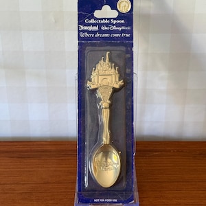 Può includere: Un cucchiaio da collezione in metallo dorato nella confezione originale. Il manico presenta un design a castello con il testo EST. 1971. La parte concava è impressa con il logo Walt Disney World. La confezione include il testo Where dreams come true.