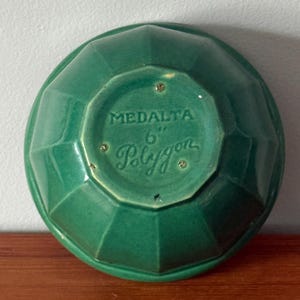 May include: A green ceramic bowl with a faceted, polygon-shaped exterior. The underside features the embossed text MEDALTA 6" Polygon, indicating a 15.24 cm diameter. The bowl has a glossy finish and a distinct geometric design with multiple flat panels.