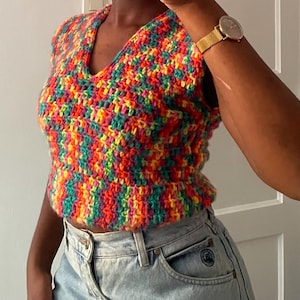 Puede incluir: Un top sin mangas de crochet arcoíris con cuello en V. El top está hecho con una variedad de colores, incluyendo rojo, naranja, amarillo, verde, azul y morado.