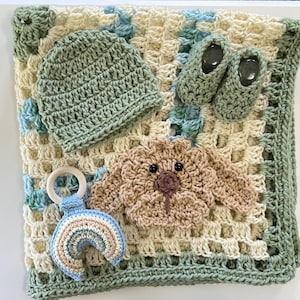 May include: A crocheted baby set featuring a blanket, hat, and booties in shades of green, cream, and blue. A crocheted toy with a wooden ring and a teddy bear applique are also included. The blanket measures approximately 24 inches square.