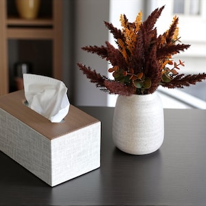 Rectangular PU leather tissue box cover with linen‑style beige texture and stitched wooden top, designed to fit standard Kleenex rectangular boxes. Features a modern, minimalist look that blends seamlessly with home décor styles from contemporary to boho. Durable magnetic closure allows easy tissue replacement, while the elegant design makes it perfect for bathroom, bedroom, living room, or office use. A stylish and functional home accessory or thoughtful gift idea.