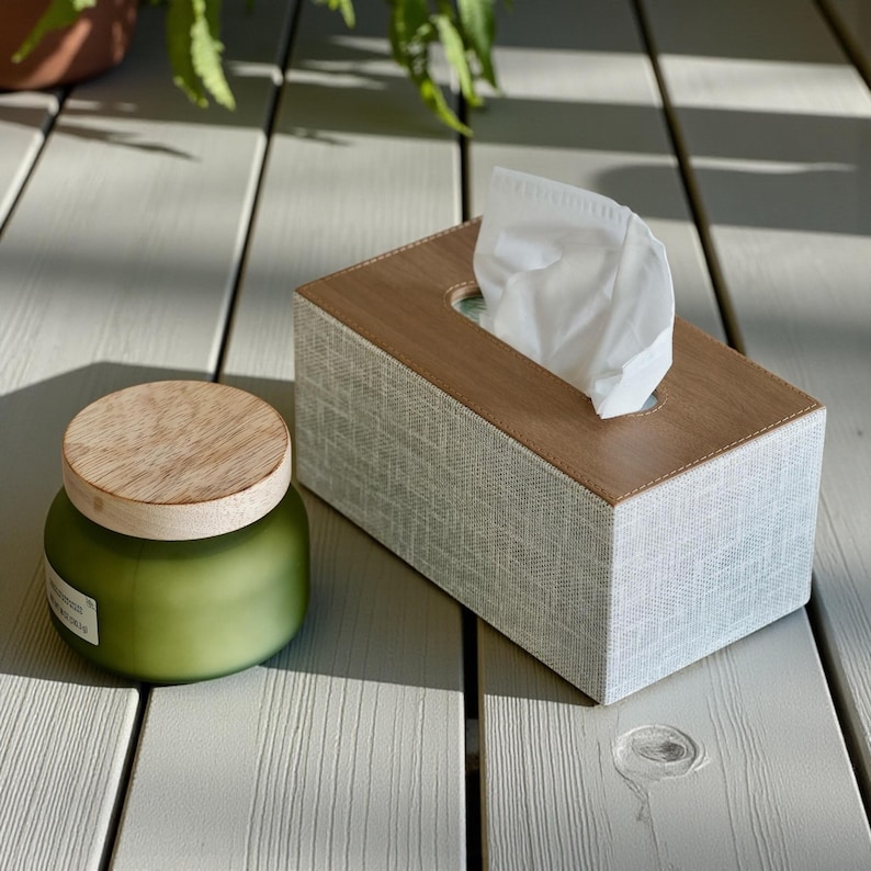 Rectangular PU leather tissue box cover with linen‑style beige texture and stitched wooden top, designed to fit standard Kleenex rectangular boxes. Features a modern, minimalist look that blends seamlessly with home décor styles from contemporary to boho. Durable magnetic closure allows easy tissue replacement, while the elegant design makes it perfect for bathroom, bedroom, living room, or office use. A stylish and functional home accessory or thoughtful gift idea.