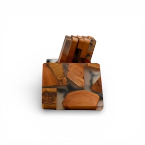 K&ouml;nnte beinhalten: Ein quadratisches Untersetzer-Set aus Holz mit einem einzigartigen Design. Die Untersetzer bestehen aus Holzst&uuml;cken, die in klarem Harz eingesetzt sind. Das Set enth&auml;lt einen Halter mit &auml;hnlichem Design. Das Holz hat eine warme, nat&uuml;rliche Farbe.