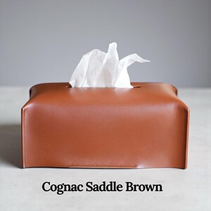 A rectangular, light gray tissue box cover with a textured surface. A white tissue is pulled from the top opening. The cover has a simple, modern design, suitable for home or office use. This is purely made with designer quality Genuine Leather.