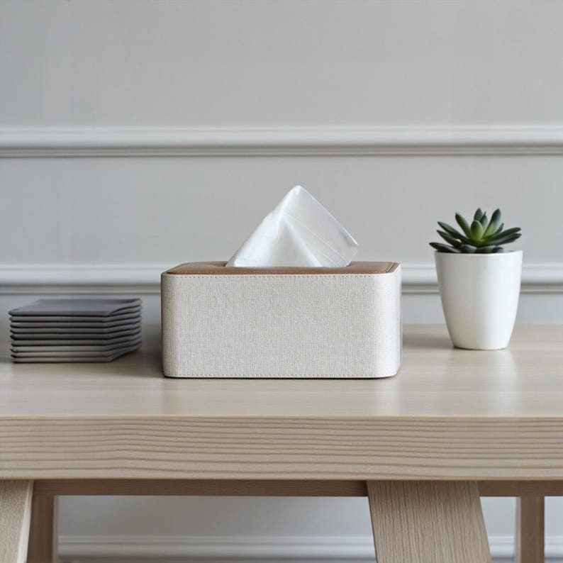 Rectangular PU leather tissue box cover with linen‑style beige texture and stitched wooden top, designed to fit standard Kleenex rectangular boxes. Features a modern, minimalist look that blends seamlessly with home décor styles from contemporary to boho. Durable magnetic closure allows easy tissue replacement, while the elegant design makes it perfect for bathroom, bedroom, living room, or office use. A stylish and functional home accessory or thoughtful gift idea.