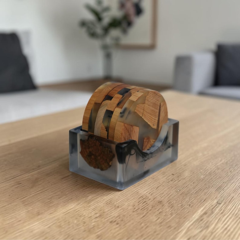 K&ouml;nnte beinhalten: Ein Set aus Holzuntersetzern mit einem transparenten Harzsockel. Die Untersetzer bestehen aus Holzscheiben und werden in einem rechteckigen Harzhalter aufbewahrt. Das Holz hat eine nat&uuml;rliche Maserung und Farbe, das Harz ist klar.