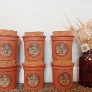 Puede incluir: Seis tarros de especias de color terracota con tapas de corcho. Cada tarro tiene una etiqueta blanca con el texto "Val do Sol" y "Spices" impreso en ella. Los tarros están dispuestos en dos filas de tres.