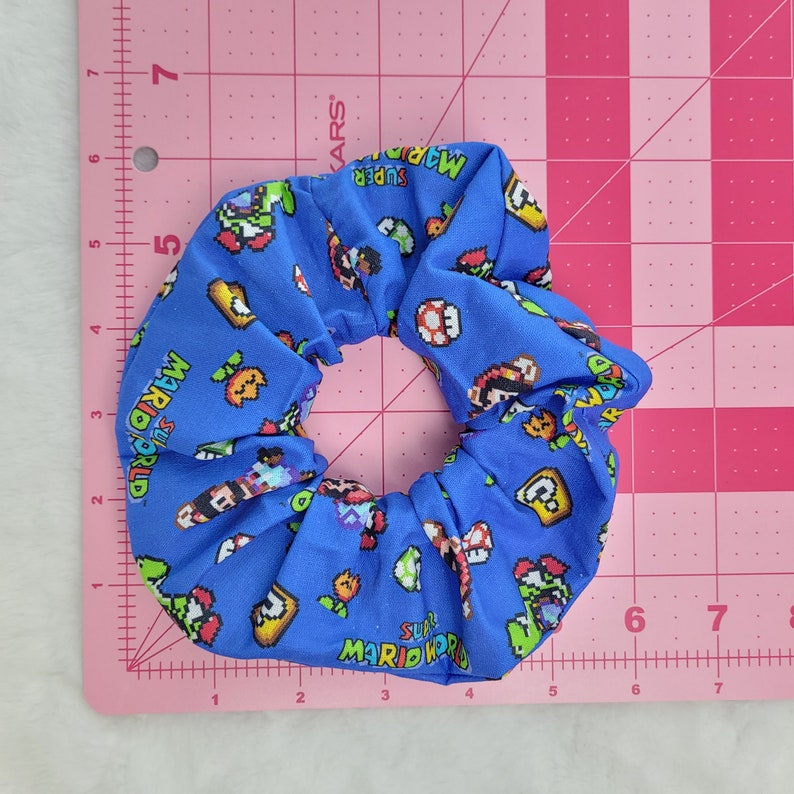 Pu&ograve; includere: Un elastico per capelli blu con un motivo di Super Mario World. L'elastico presenta vari personaggi e oggetti del gioco, tra cui Mario, Luigi, Yoshi e Goomba.