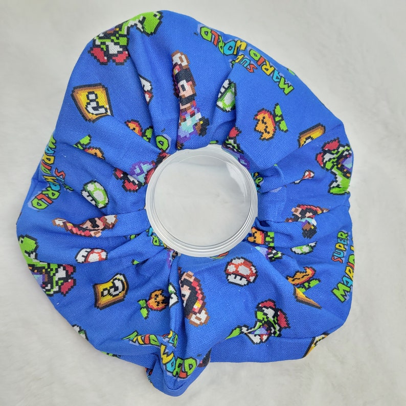 Pu&ograve; includere: Un impacco di ghiaccio in tessuto blu a tema Super Mario World. L'impacco di ghiaccio presenta vari personaggi e oggetti del videogioco Super Mario World, tra cui Mario, Luigi, Yoshi e i Goomba.