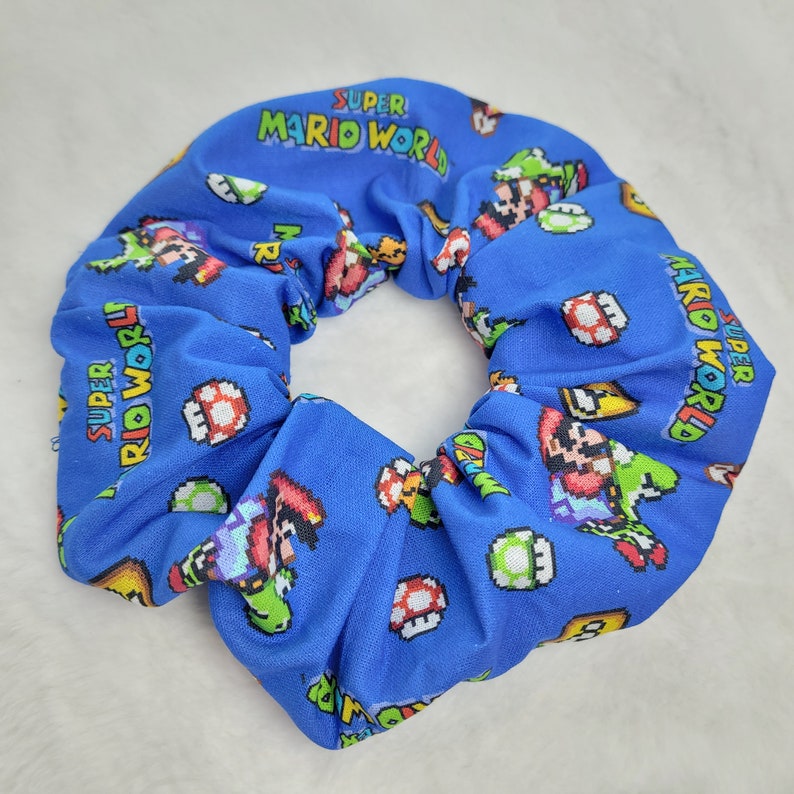 Pu&ograve; includere: Un elastico per capelli in tessuto blu con un motivo ripetuto di personaggi e oggetti di Super Mario World, tra cui Mario, Luigi, Yoshi, Goomba e funghi.