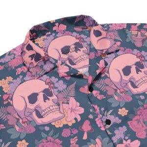 Puede incluir: Una camisa azul de botones con estampado floral y de calavera. La camisa tiene un estampado floral rosa y blanco con calaveras rosas y setas. El texto "SLEEP LESS" es visible en el cuello.