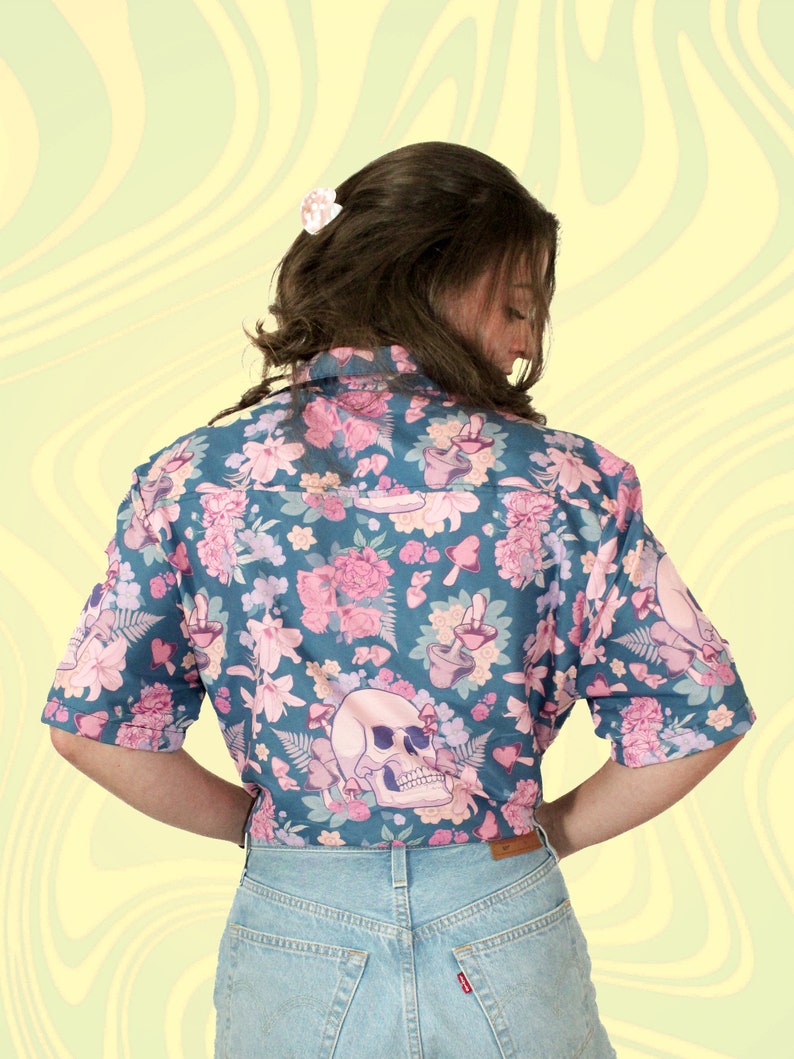 Puede incluir: Una camisa de botones de manga corta azul verdosa con estampado floral con flores rosas, setas y una calavera.