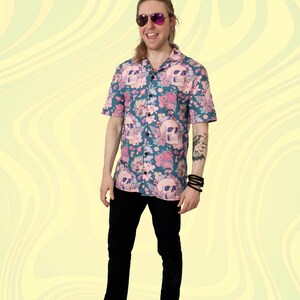 Puede incluir: Un hombre con una camisa de manga corta azul y rosa con botones, con un estampado de calavera y flores. Lleva pantalones negros y zapatillas negras y blancas. Tambi&eacute;n lleva gafas de sol.