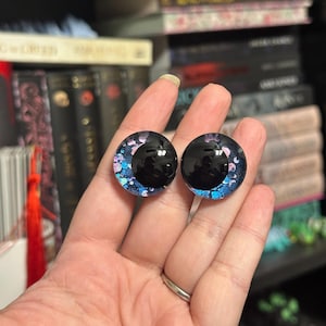 May include: A pair of black and blue glass eyes with iridescent glitter. The eyes have a black pupil and a white iris with pink and blue glitter.