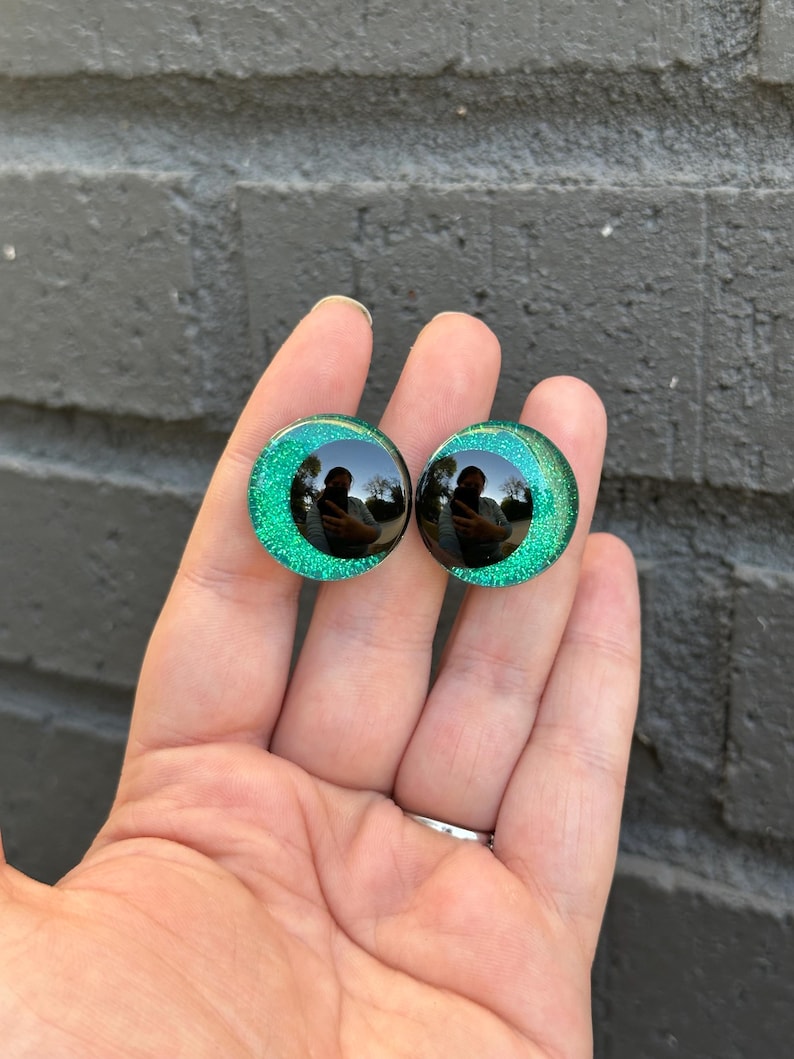 May include: Two green glitter round plastic eyes with black pupils. The eyes are about 1 inch in diameter.