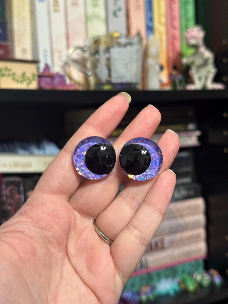 May include: Two purple and black glass eyes with glitter accents. The eyes are round and have a black pupil.
