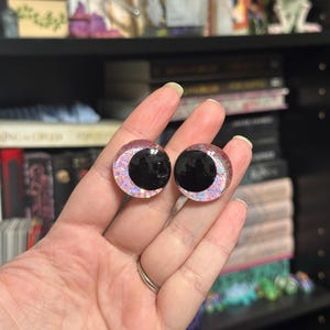 May include: Two black and pink iridescent plastic eyes with a black pupil. The eyes are round and have a shiny finish.