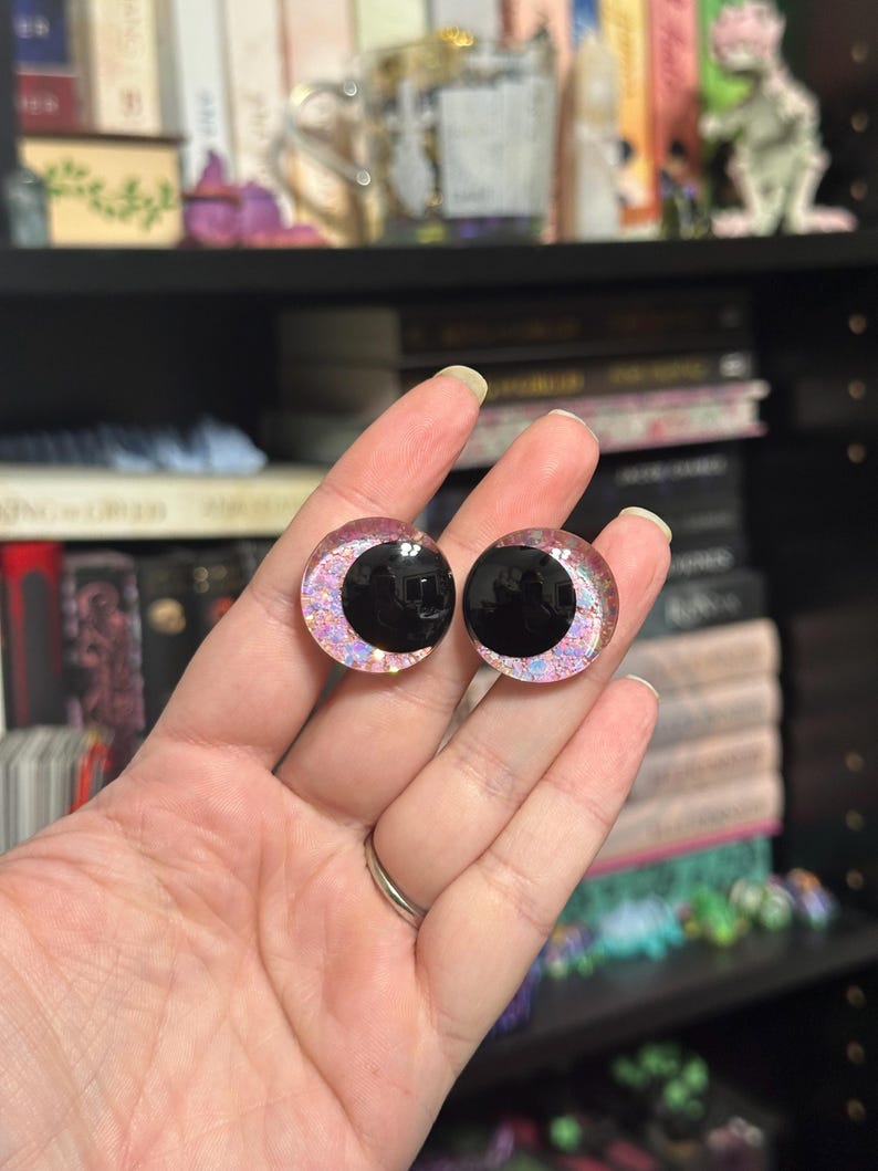 May include: Two black and pink iridescent plastic eyes with a black pupil. The eyes are round and have a shiny finish.