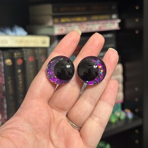 May include: Pair of black and purple glitter doll eyes with a black pupil. The eyes are round and have a glossy finish.