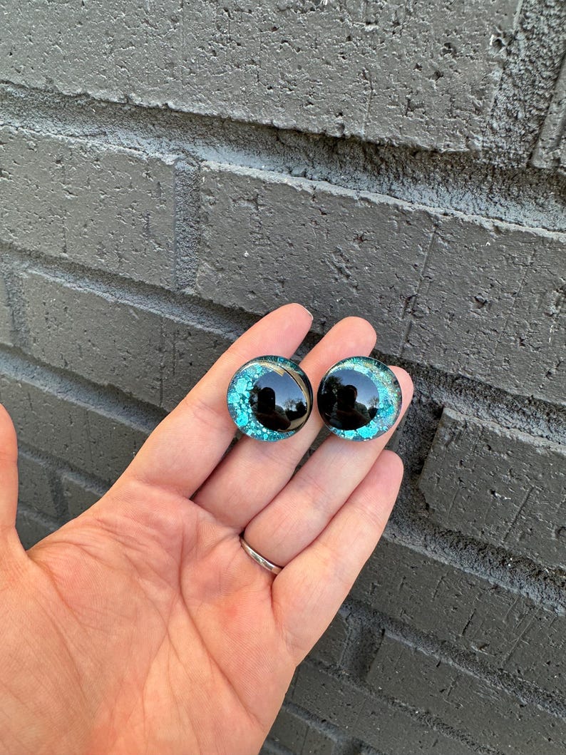 May include: Two round, black, plastic eyes with a turquoise glitter finish. The eyes are about 1 inch in diameter.