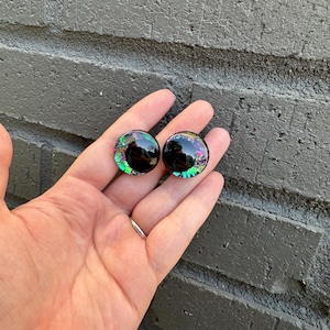 May include: A pair of black and green glitter round googly eyes with a black pupil.
