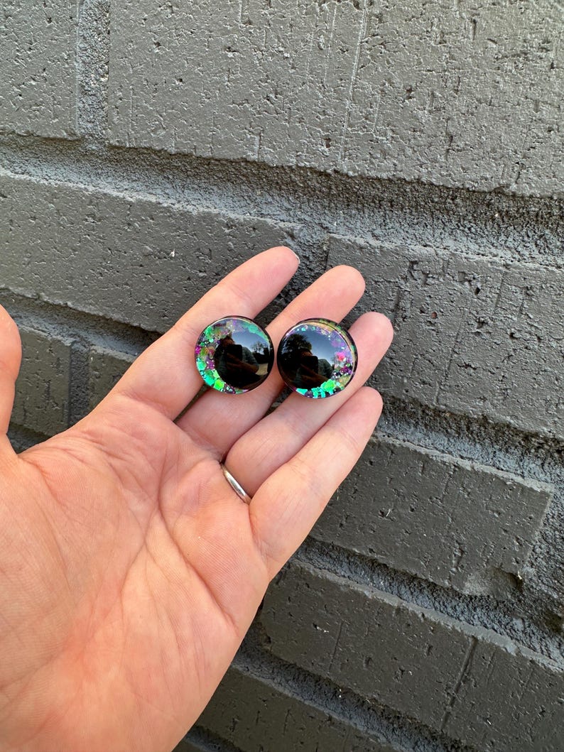 May include: A pair of black and green glitter round googly eyes with a black pupil.