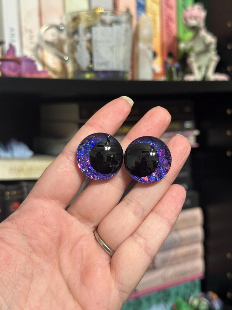 May include: Two round, black-pupil, glass eyes with a purple and blue glitter rim. The eyes are approximately 2.5 cm in diameter.