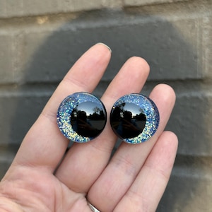 May include: Two black and blue glitter safety eyes with a black pupil. The eyes are round and have a shiny finish.