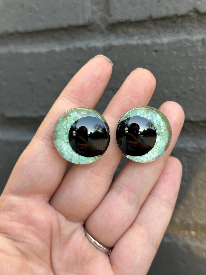 May include: Two round, green and black glass eyes with a black pupil. The eyes are for crafts and are about 1 inch in diameter.