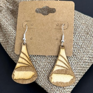 May include: Wooden drop earrings featuring a light-colored map of Puerto Rico, set against a fan-like design. The earrings are attached to silver-colored hooks and displayed on a brown card, with a burlap bag in the background.