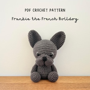 May include: A handmade gray crochet French Bulldog, with black eyes and nose, sitting on a wooden surface. The text "PDF Crochet Pattern" and "Frankie the French Bulldog" are above the dog. The dog has large, upright ears.